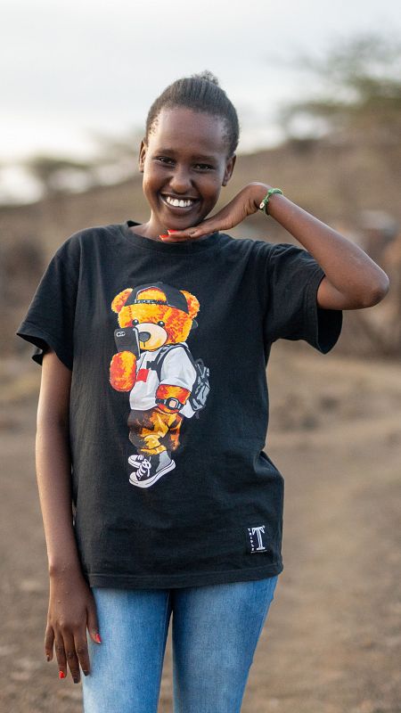 Una joven africana con camiseta negra sonríe haciendo un gesto con su mano sujetando su cara.