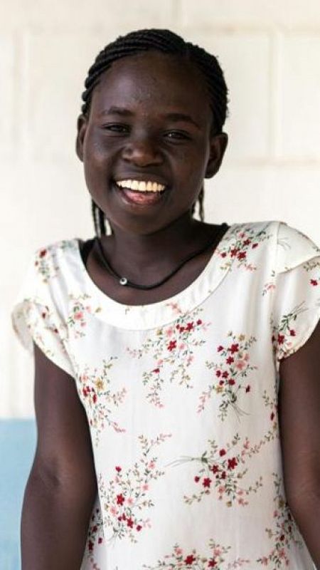 Una joven africana con vestido blanco de flores y peinado recogido de trenzas sonríe a la cámara.
