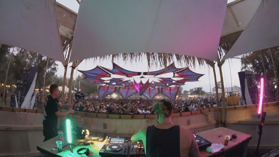 Un dj pincha música y jóvenes bailan bajo una carpa de festival