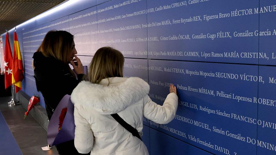 Dos mujeres se acercan al panel con los nombres de las víctimas del 11M instalado en Atocha por el 20 aniversario