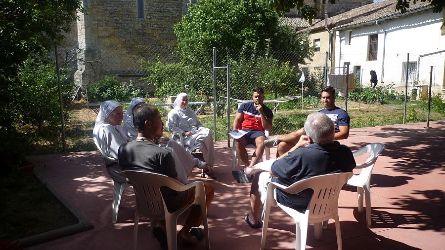 Hombres y mujeres sentados al aire libre con una casa de pueblo detrás