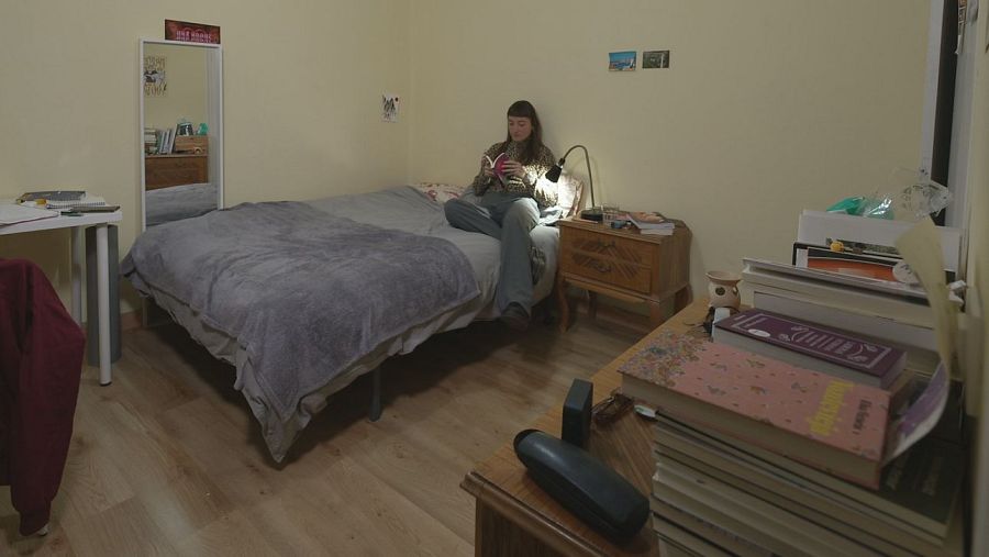 Una chica lee un libro sentada en la cama.