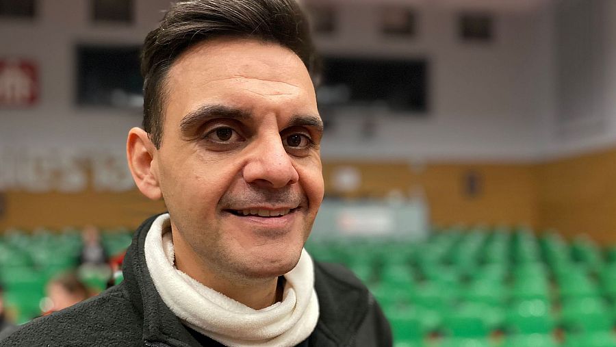 Un hombre con sillas verdes desenfocadas en el fondo.