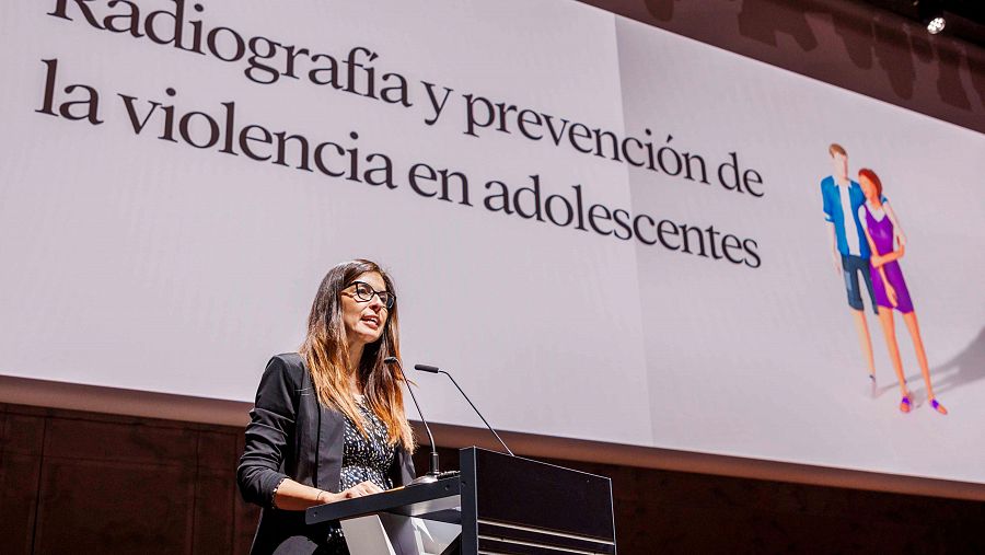 Una mujer en un atril con una diapositiva detrás en una presentación
