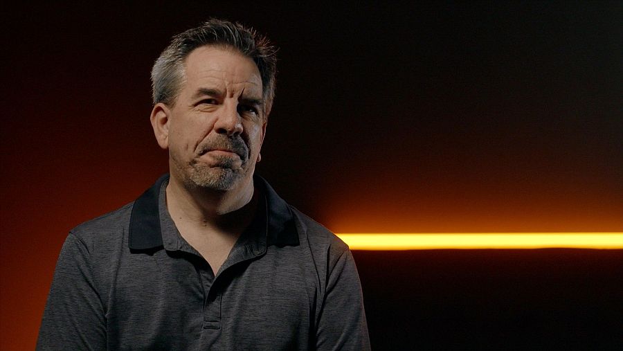 Hombre con barba sobre fondo negro y una barra horizontal luminosa.