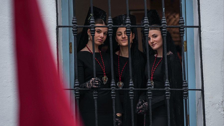 Tres hermanas de la Caridad miran desde la ventana antes de la suspensión por lluvia de su estación de penitencia este Jueves Santo en Córdoba