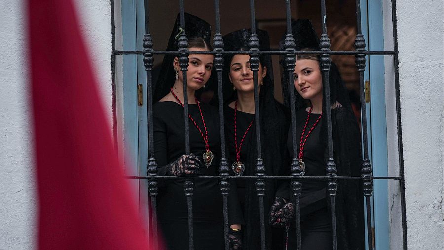 Tres hermanas de la Caridad miran desde la ventana antes de la suspensión por lluvia de su estación de penitencia este Jueves Santo en Córdoba