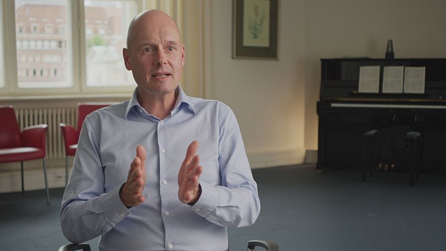 Hombre calvo sentado en una sala moviendo las manos