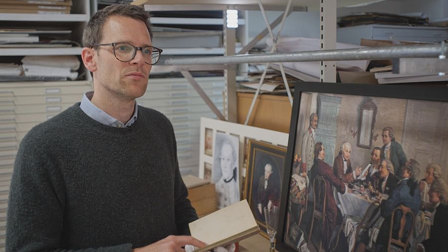 Hombre con gafas , jersey gris oscuro y con libro en las manos.