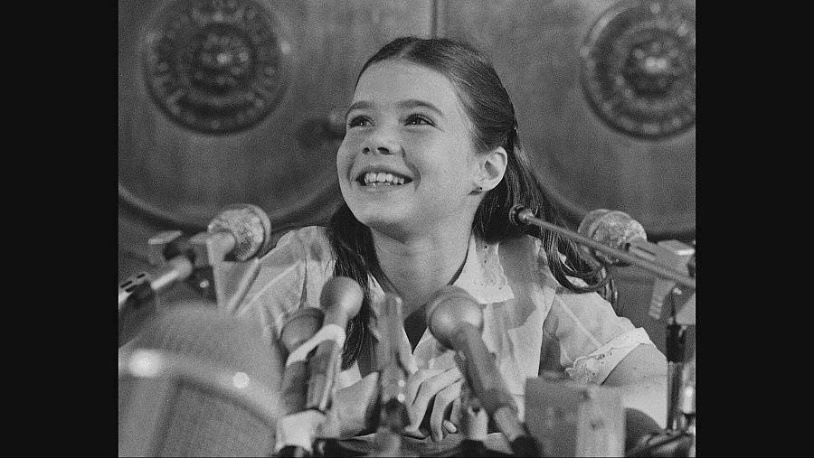 Foto en blanco y negro de una niña delante de varios micrófonos
