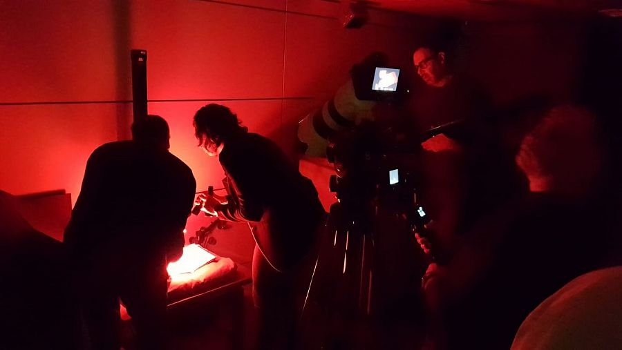 Un equipo de TVE graba a dos técnicos en un laboratorio de fotografía con luz roja.