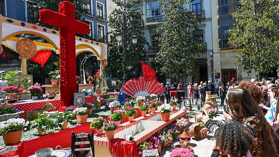 Varias personas observan una de las cruces que adornan las principales plazas y barrios de Granada