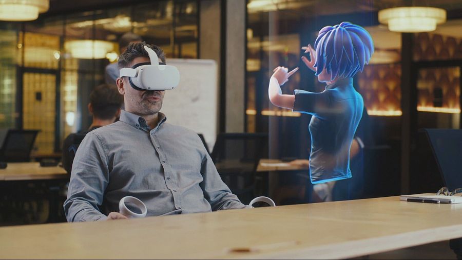 hombre con gafas inmersivas delante de un ordenador y una asistente virtual
