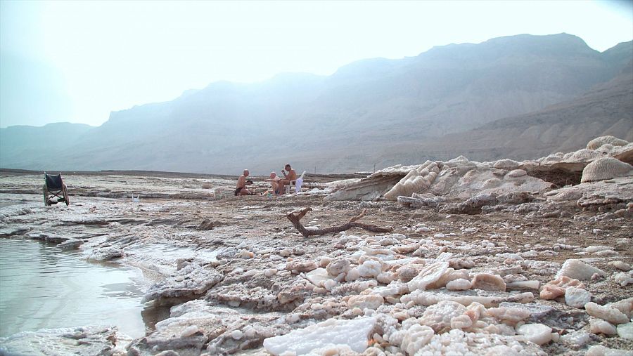 tres hombres en bañador a orilla de mar sentados conversan