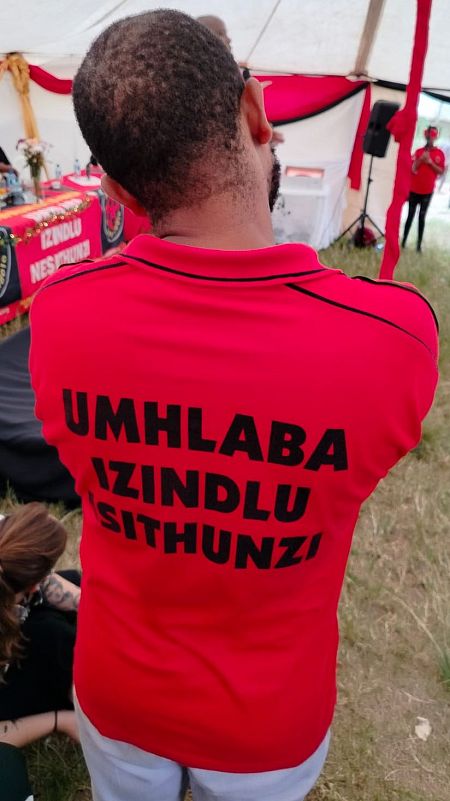 Thapelo Mohapi, de espaldas, durante una asamblea en Shaka's Head con una camiseta en la que puede leerse “Tierra, Vivienda y Dignidad”