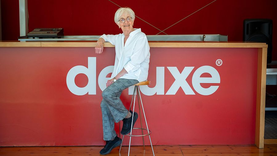 Maria Lluïsa Solà asseguda a un tamboret davant d'una barra amb les lletres deluxe