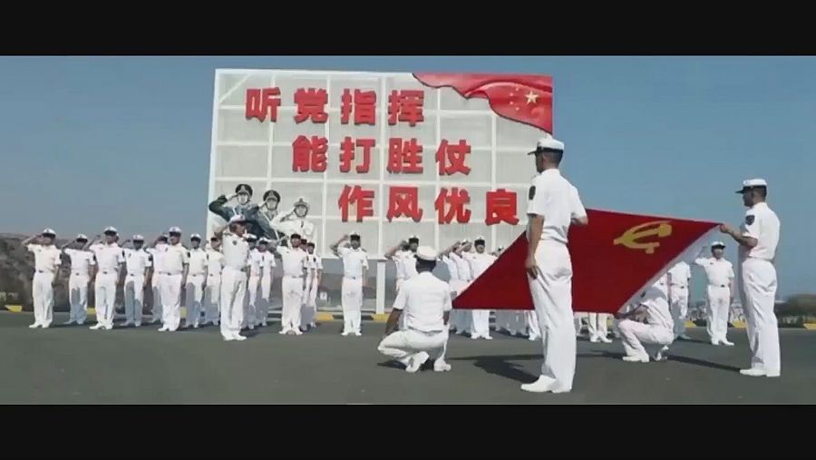 Soldados del ejército chino saludando con bandera y una pantalla con palabras en chino