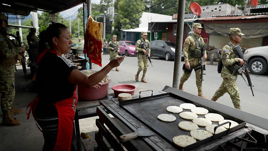 Una mujer prepara tortillas mientras militares patrullan en las calles de El Salvador