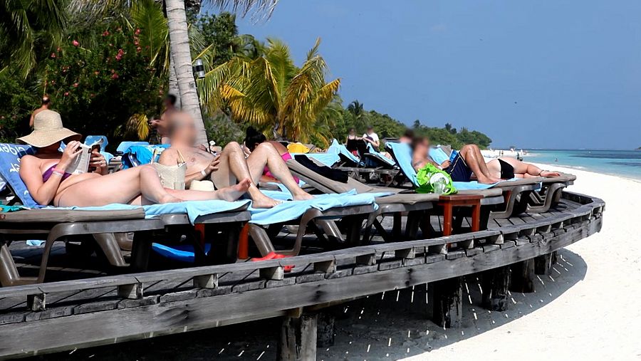 turistas sentados en sillas en la playa de arena blanca y mar turquesa