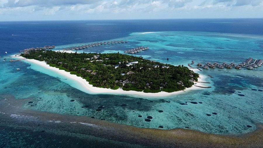 Isla verde rodeada de arena blanca y agua turquesa con bungalós sobre el mar