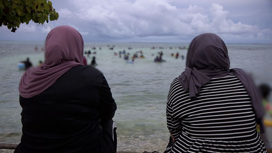 Dos mujeres de espaldas con velo miran desde la playa a los bañistas