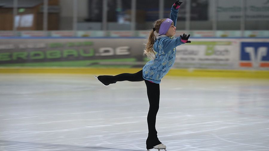 niña con pantalón negro y chaqueta azul patinando sobre hielo