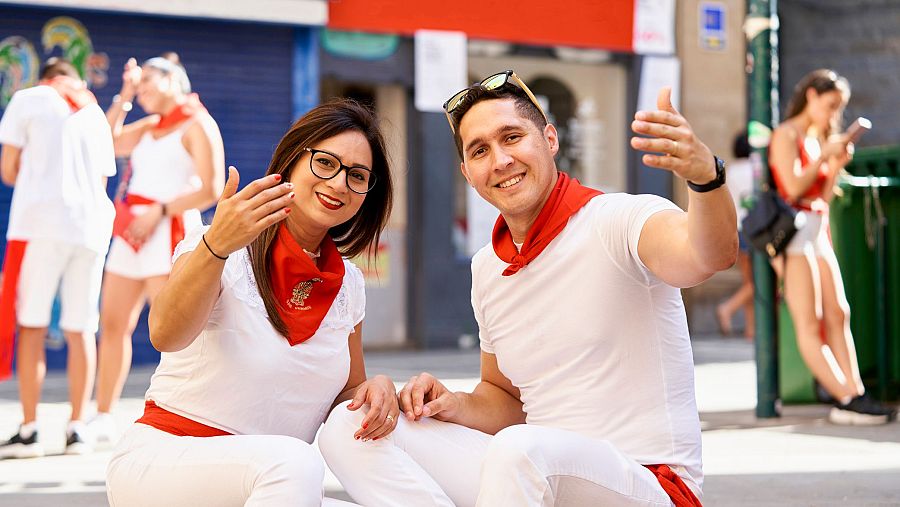 Un chico y una chica vestidos con el traje de San Ferín hacen un gesto de acogida.