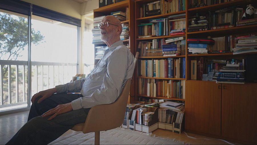 Hombre con gafas y barba sentado y con una librería llena de libros a su espalda