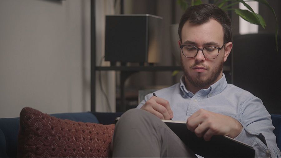 Chico joven con gafas y barba escribe en un cuaderno