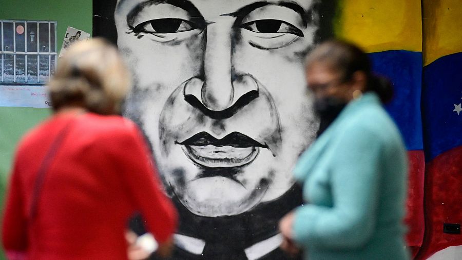 Un mural de Hugo Chávez es visto mientras unas mujeres sostienen papeletas en un colegio electoral durante las elecciones presidenciales, en Caracas.