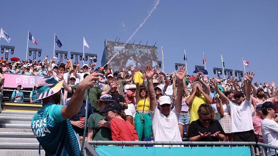 Un trabajador de los Juegos de París arroja agua a los aficionados antes de un partido de vóley playa