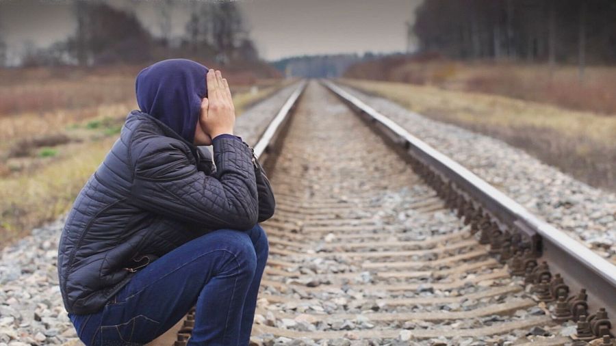 joven sentada en las vías del tren tapándose la cara con las manos