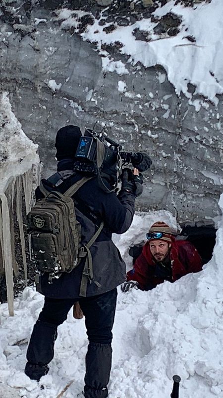 un hombre graba con una cámara a otro que sale desde una cueva glaciar