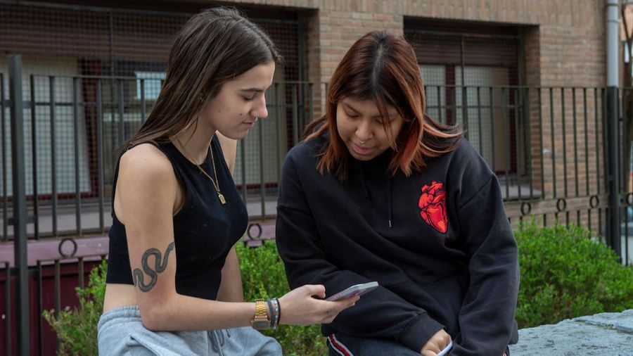 Dos chicas miran un teléfono móvil en la calle.