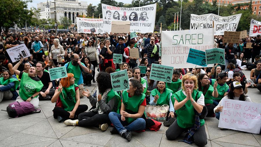 Al fondo, un cartel carga contra Sánchez, Ayuso y Yolanda Díaz durante la manifestación en Madrid