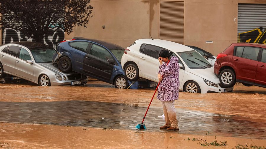 Una mujer realiza labores de limpieza junto a vehículos destrozados tras el paso de la DANA