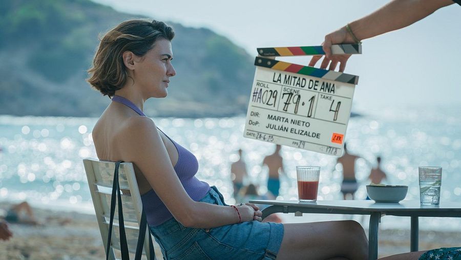 Un miembro del equipo de rodaje de 'La mitad de Ana' sostiene la claqueta mientras una actriz espera instrucciones en la playa.