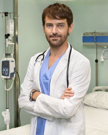 Médico con bata y estetoscopio en una habitación de hospital.