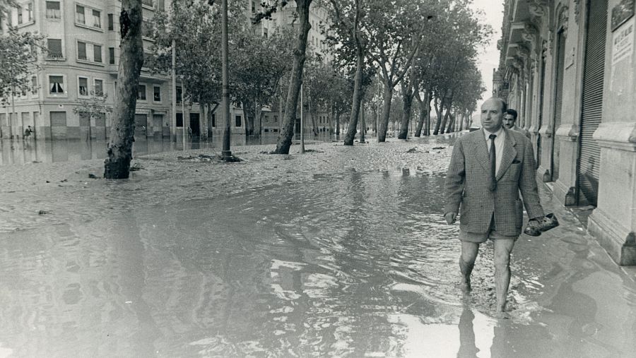 Una calle de Valencia inundada tras la riada de 1957. Un hombre camina por la calle con un zapato en la mano. 
