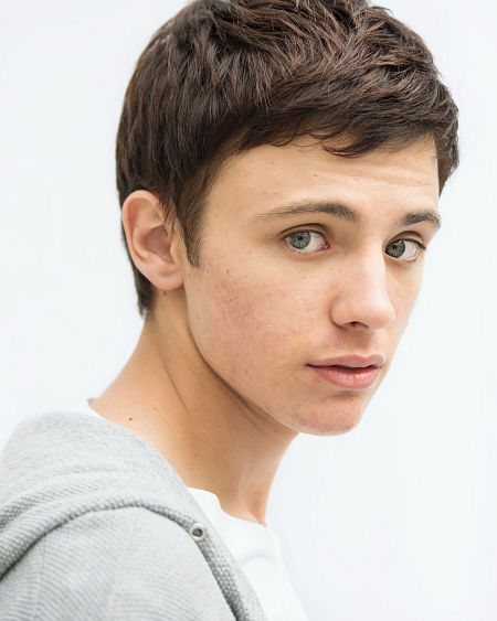 Joven con sudadera gris y camiseta blanca mira a la derecha sobre fondo blanco.