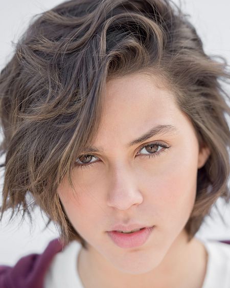 Claudia, con pelo castaño corto y despeinado, mira seriamente a la cámara.