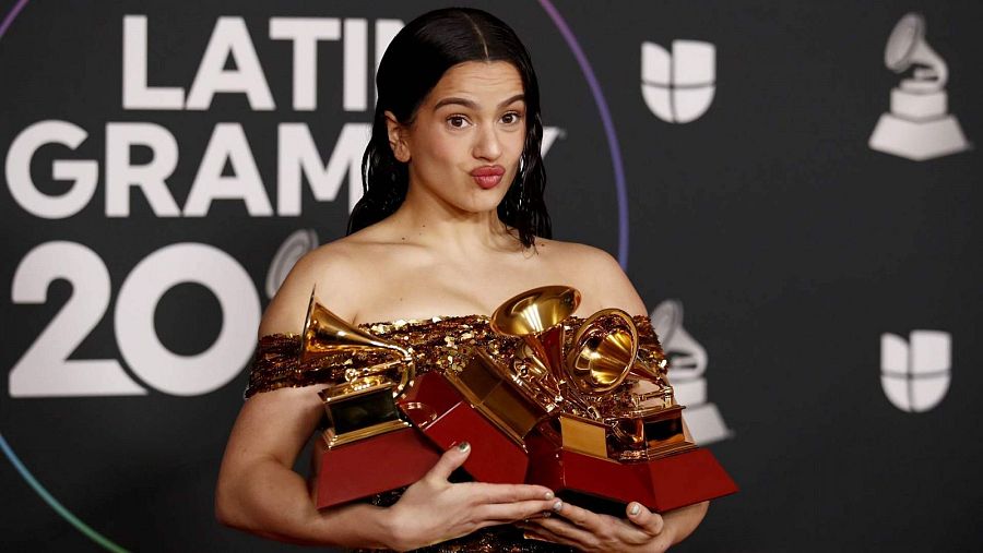 Rosalía, vestida con un brillante vestido dorado, sostiene con orgullo sus premios de los Latin Grammy 2022.