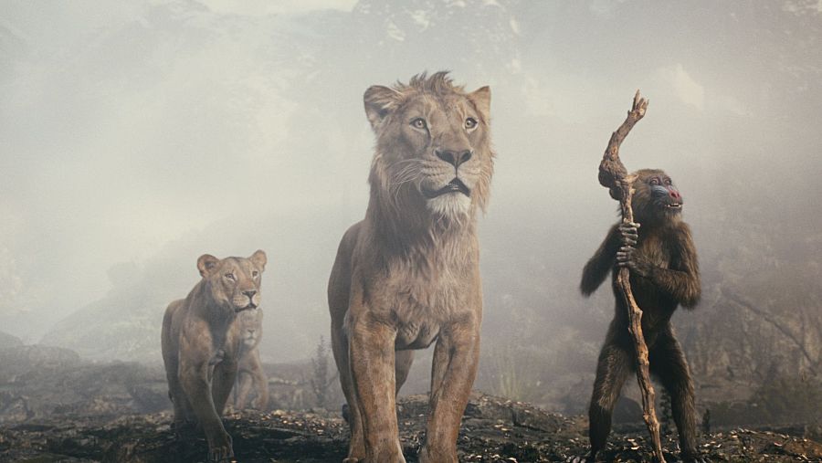 Escena de 'Mufasa: El Rey León' con un león, una leona y un mandril en un entorno rocoso y con niebla.