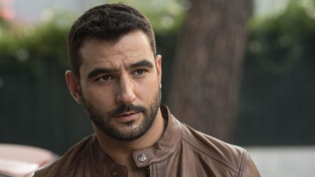 El actor Álex González mira con expresión seria, vestido con una chaqueta de cuero marrón.