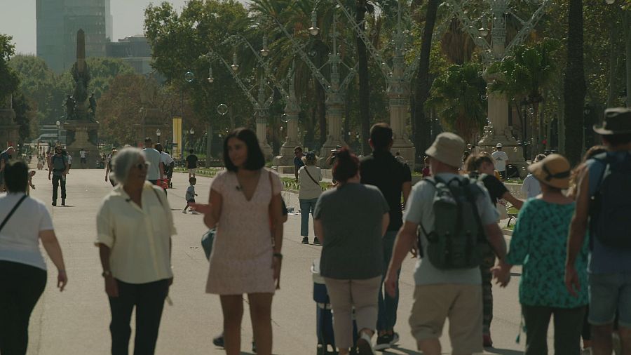 Dos mujeres pasean por un paseo de Barcelona en un día soleado con mucha gente alrededor.