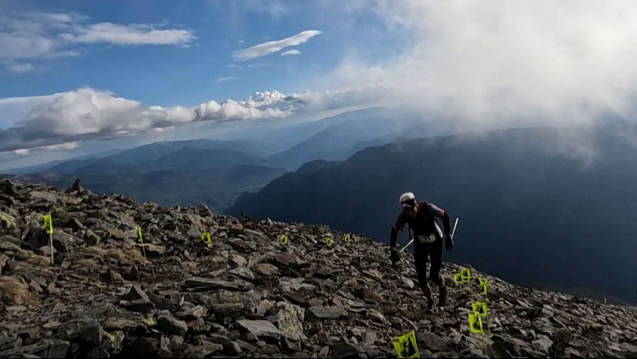 Corredor asciende por una rocosa cima del Pirineo, con banderas amarillas marcando el camino.