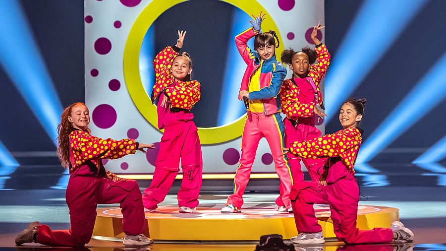 Chloe DelaRosa ensaya con sus bailarinas en el escenario de Eurovisión Junior, con un fondo de lunares y un círculo amarillo.