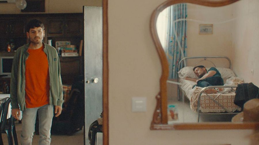 En un fotograma de 'Por donde pasa el silencio', un hombre observa el reflejo de otro hombre durmiendo en una cama.