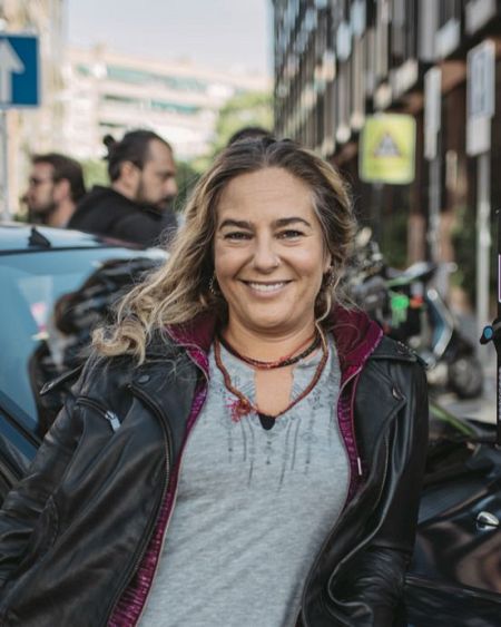 Inés Hernand, con chaqueta de cuero y camiseta gris, sonríe en un ambiente urbano.