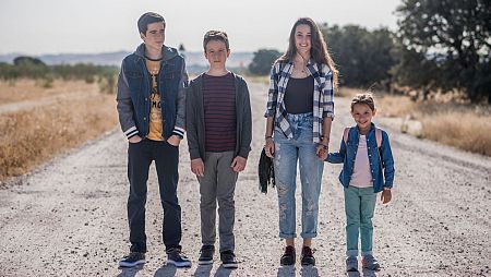 Cuatro hermanos caminan de la mano por un camino rural, mostrando unidad familiar.